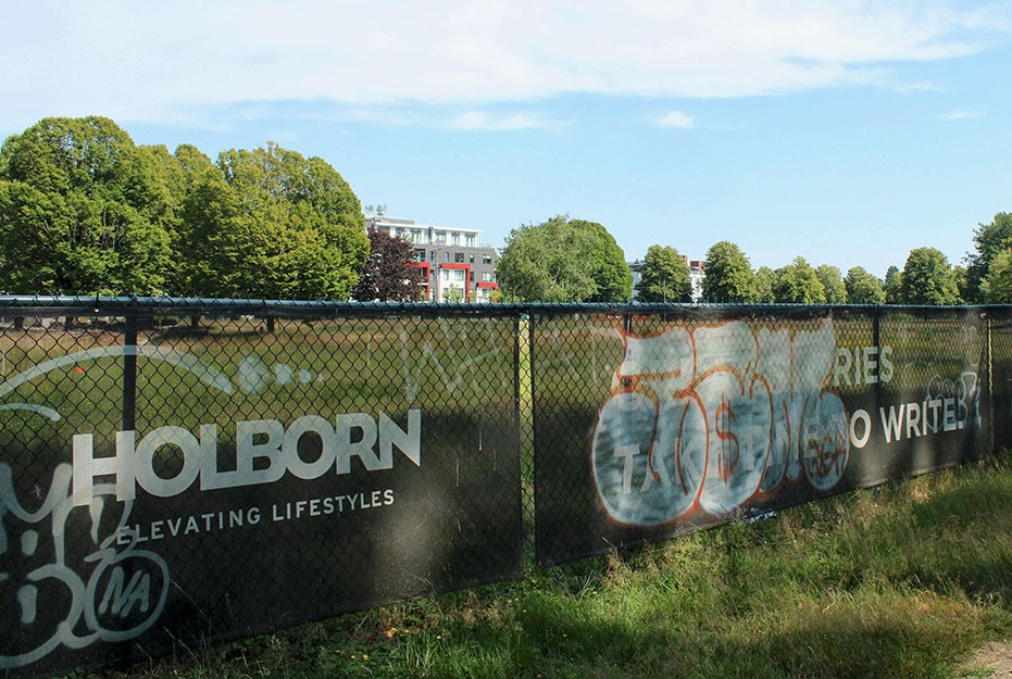 A chain link fence adorned with Holborn advertising banners that say &ldquo;Great Stories Take Time to Write&rdquo; and graffiti.