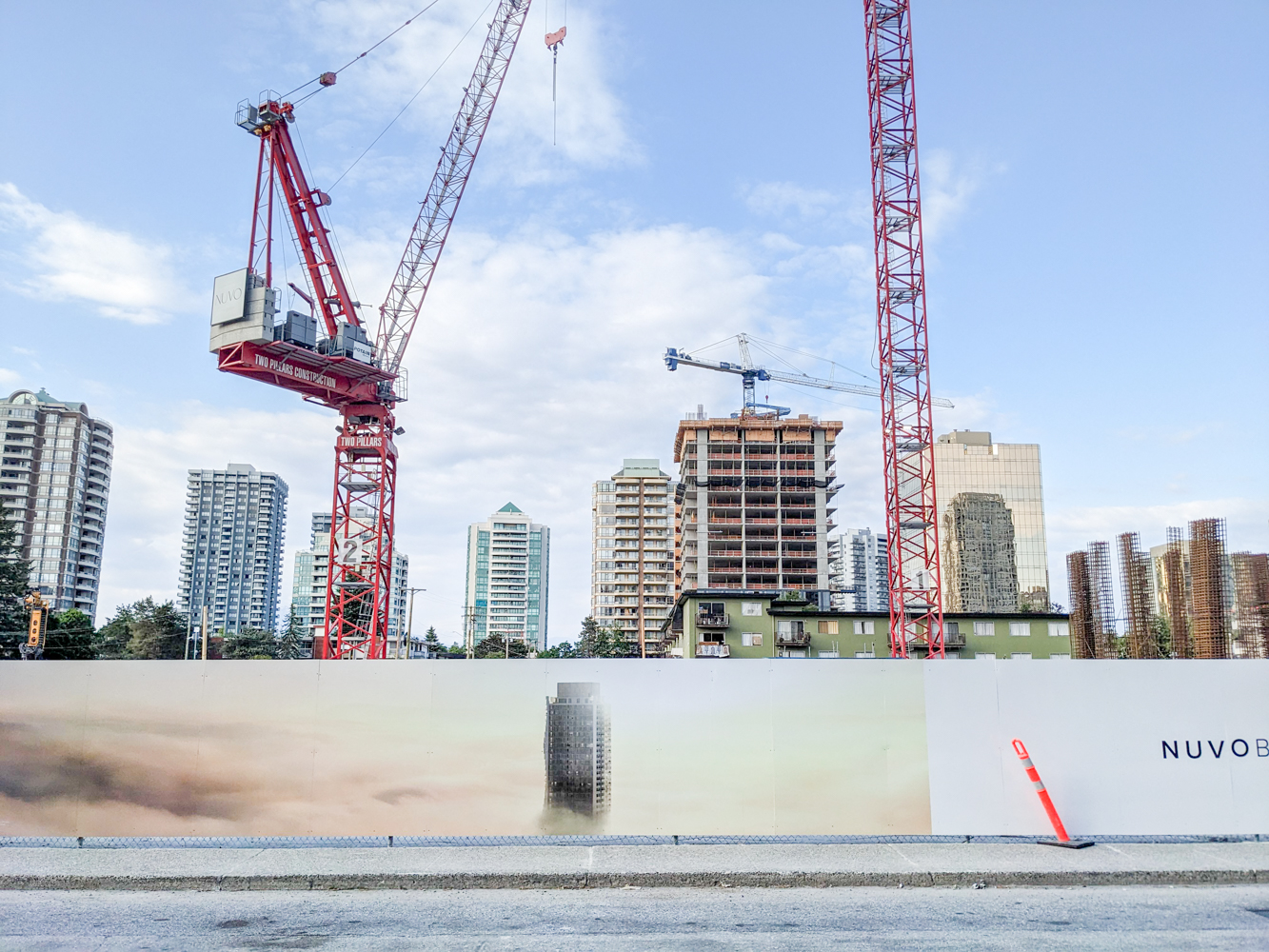 The image of a tower on a fence. Behind it are cranes. Behind the cranes are an urban skyline.