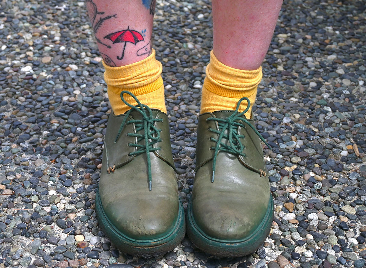 A close up of Alex&rsquo;s green leather shoes. She has a tattoo of a red umbrella that represents sex worker advocacy. 