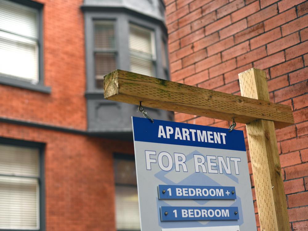 A red brick apartment building with a for-rent sign.