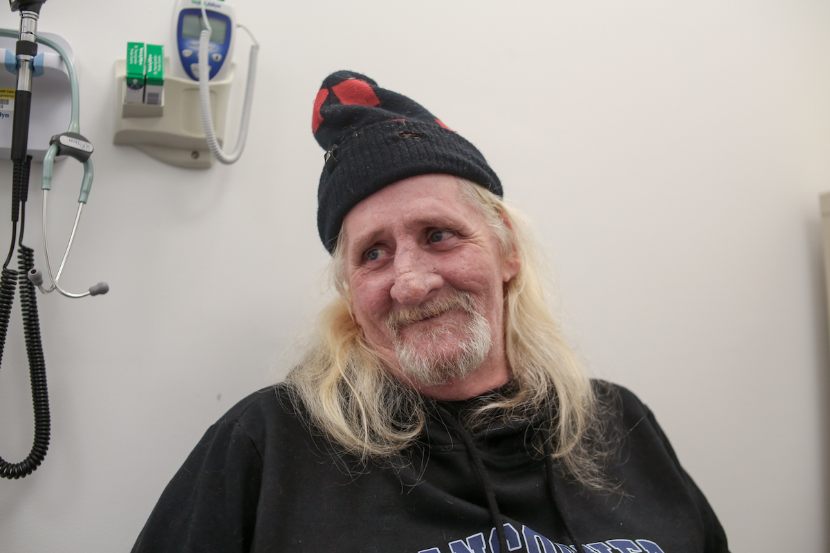 A man wears a tuque. He is smiling at someone off-camera.