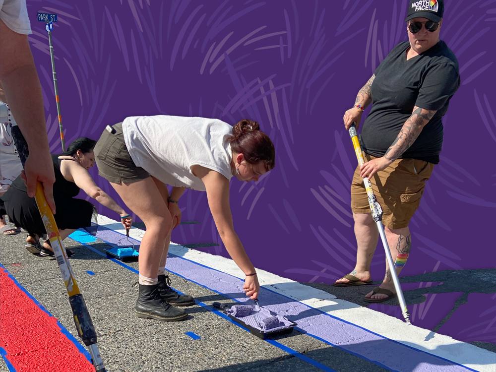People paint a rainbow crosswalk on the ground.