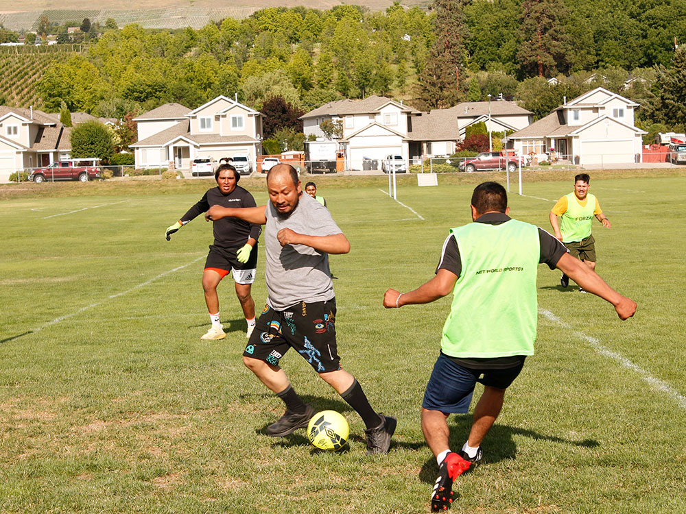 Five men play soccer in a grassy field.