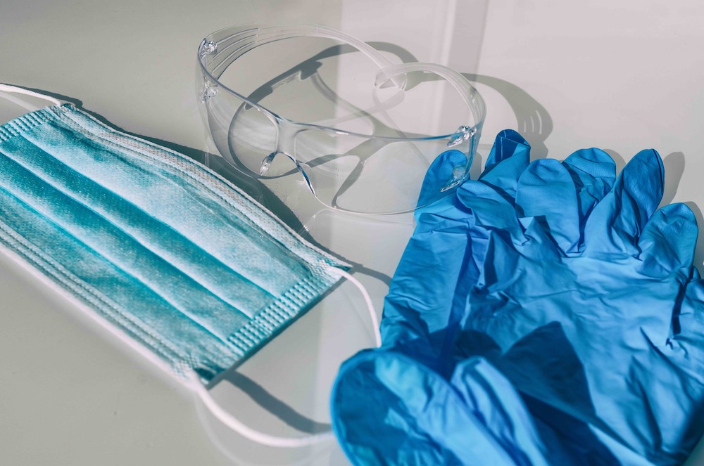 A mask, safety goggles and gloves sit on a counter.