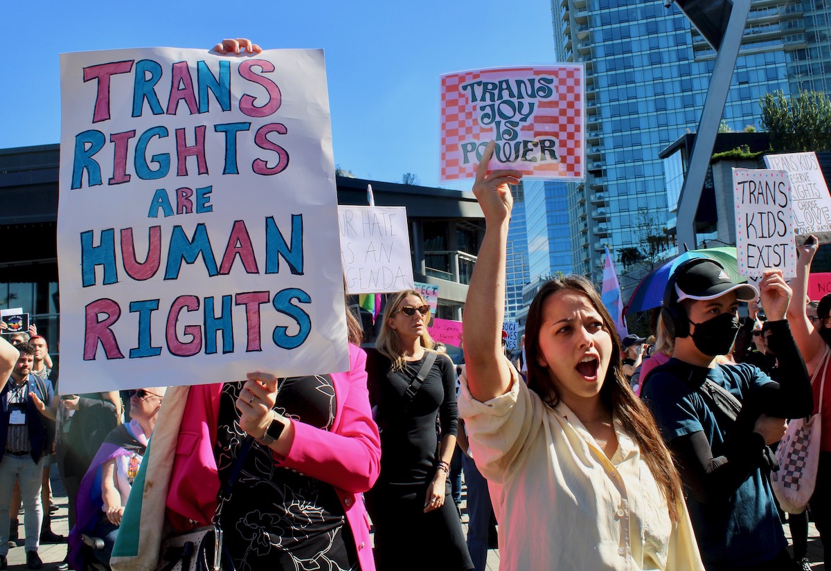 People hold up ‘Trans rights are human rights’ signs and ‘Trans joy is power’ signs.