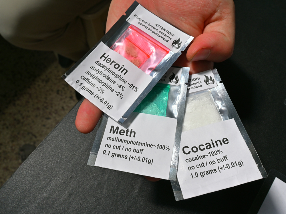 An open hand holds three small baggies labelled &lsquo;Heroin,&rsquo; &lsquo;Meth&rsquo; and &lsquo;Cocaine.&rsquo;