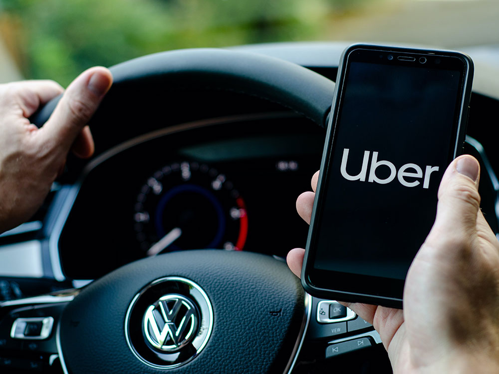The interior of a car, with the driver holding a phone with the Uber logo on the screen.