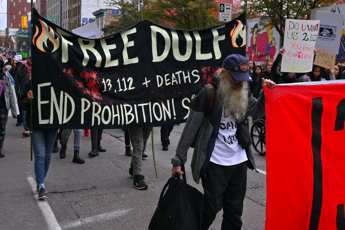 A banner at a rally reads, &lsquo;FREE DULF. 13,112+ deaths. End Prohibition!&rsquo; It is covered with red handprints.