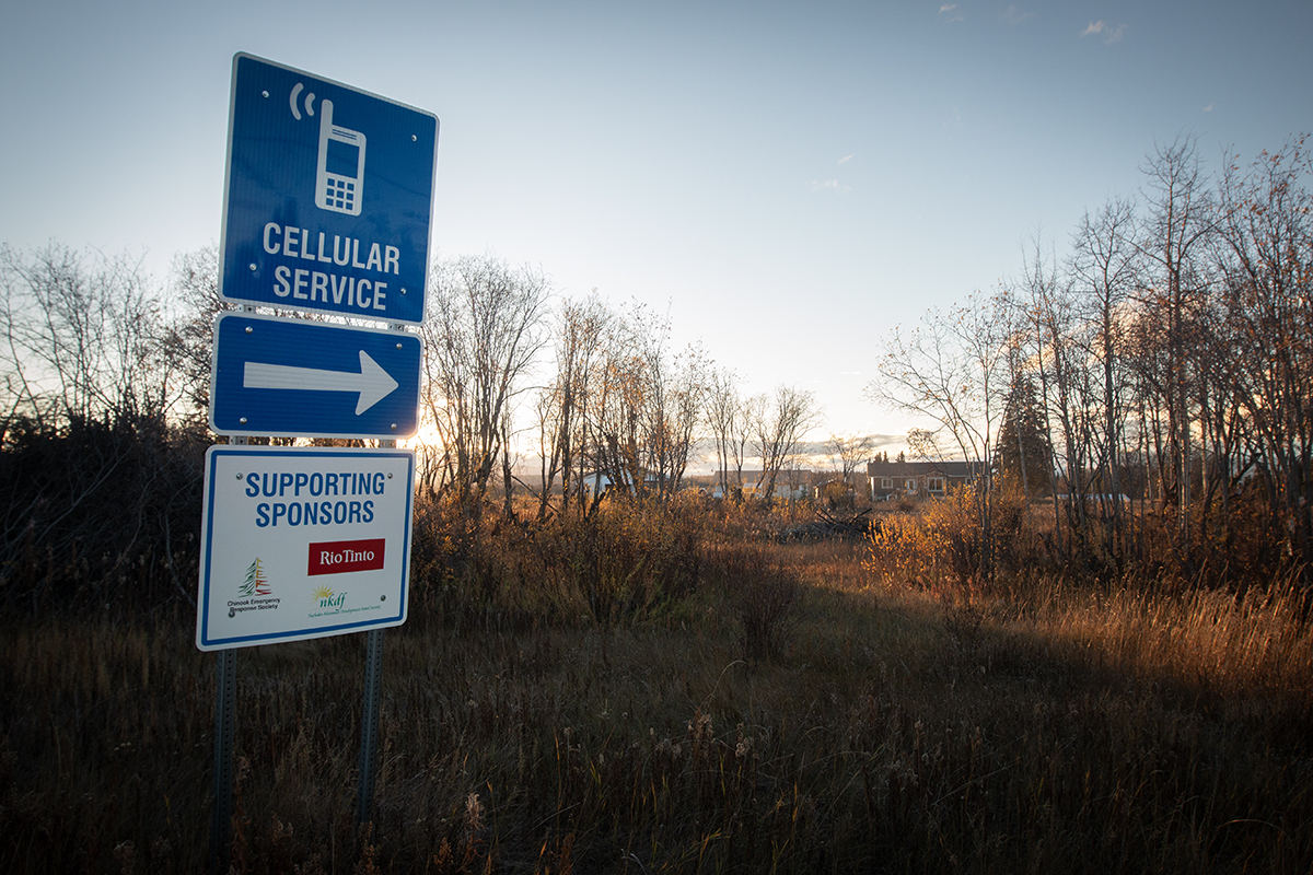 A blue sign that says 'cellular service' shows an arrow pointing to the right. The sign is backlit by a setting sun in a rural area.