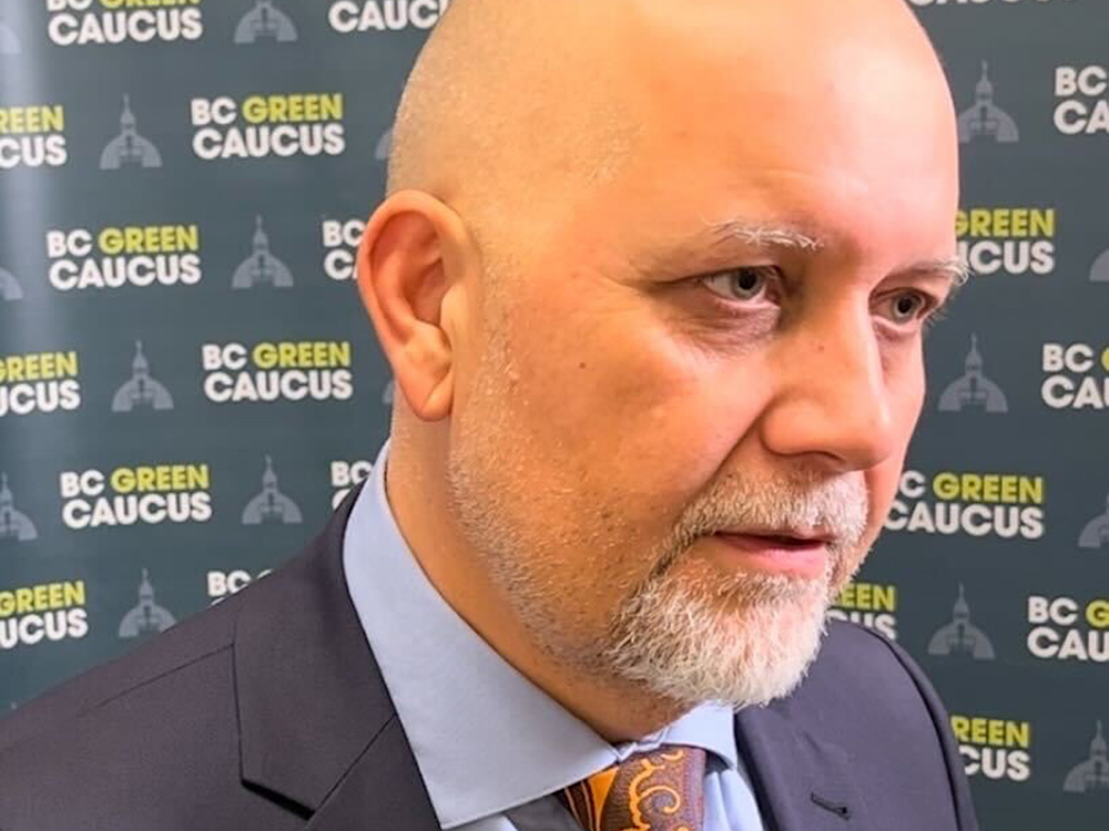 Adam Olsen, a lighter-skinned man with a close-shaven head and short beard, smiles at the camera.