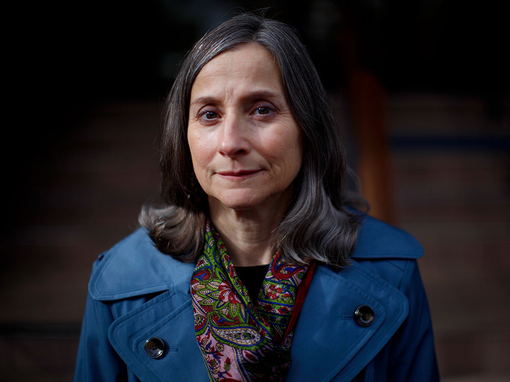 Lisa Lapointe, a white woman with grey-brown hair just past her shoulders, looks directly at the camera. The mood is sombre.