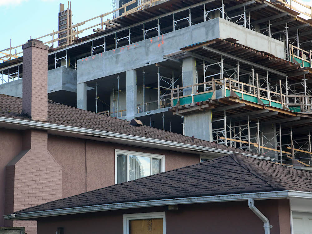 A close-up of the roof of a pink house and a concrete tower going up behind.