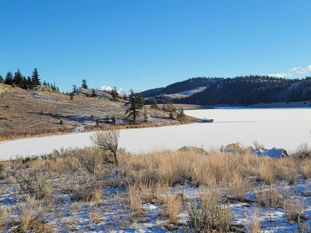 A snow-covered lake surrounded by rolling hills.