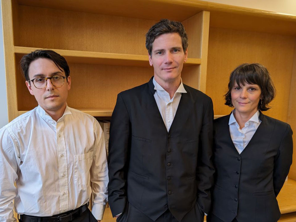 Three people in office attire stand side by side.