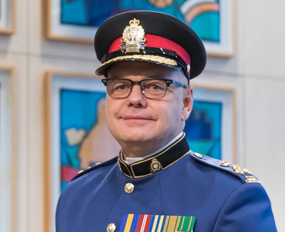 An officer with a light skin tone wears a black hat with an EPS shield and a blue jacket festooned with medals.
