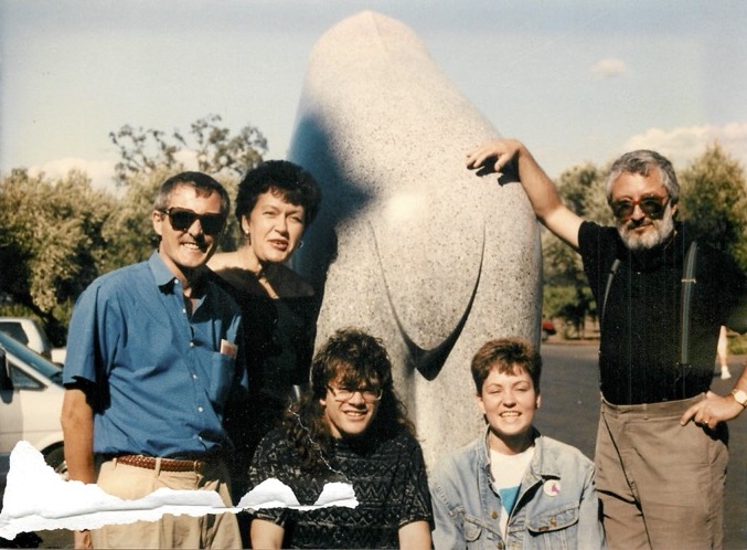Five people pose near a large granite statue in a sunny outdoor area in a film photo from 1990. They are wearing spring clothes and some are in sunglasses.
