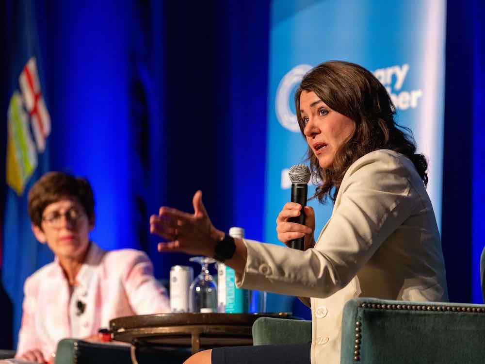 A 50-ish woman with shoulder-length dark brown hair gestures as she speaks to an audience.