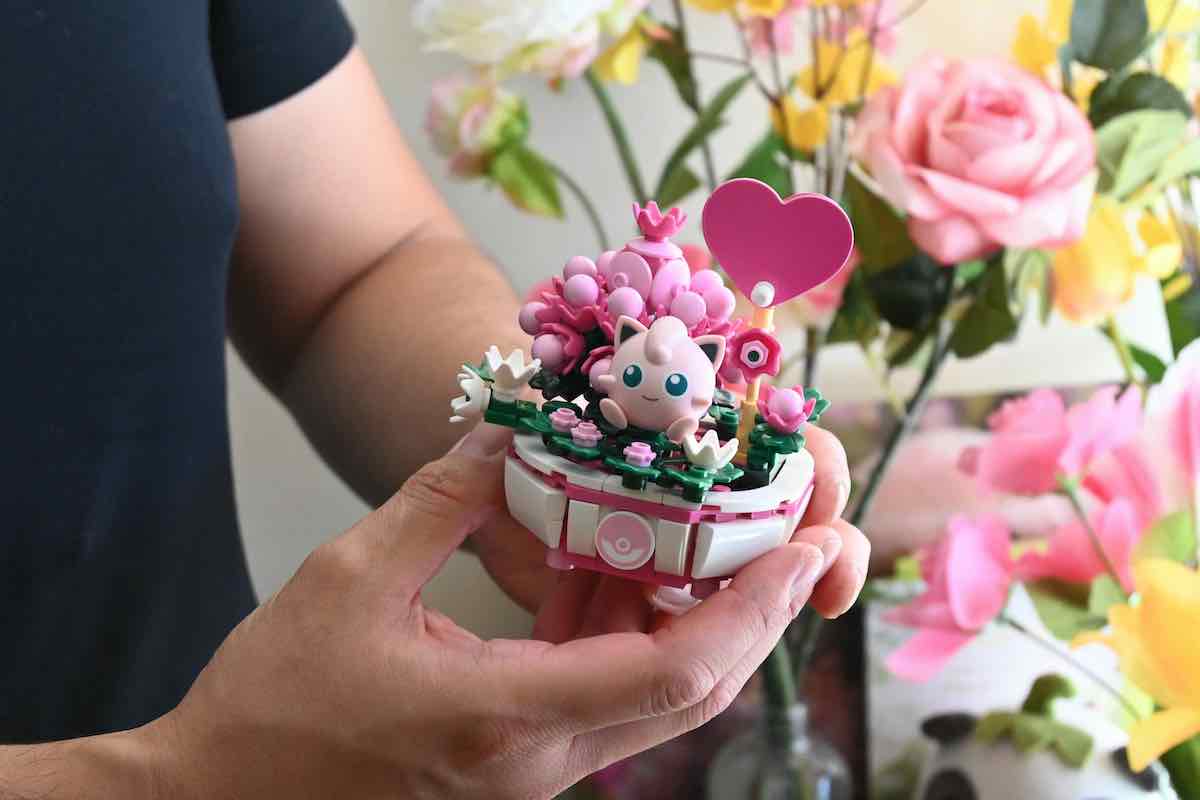 Eric Li holds a small pink and white Lego arrangement featuring flowers and a small pink cartoon character with a heart on a stick.