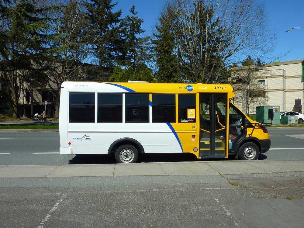 A white, yellow and blue HandyDart bus parked in Richmond, BC.