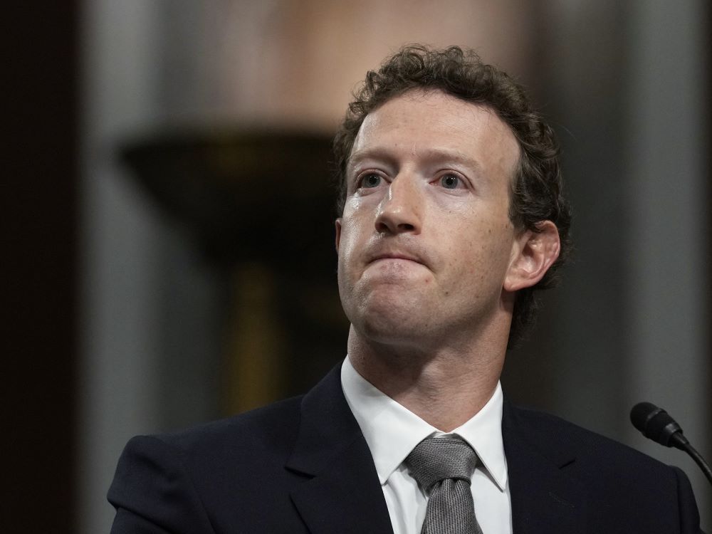 Mark Zuckerberg, a fair-skinned man with reddish curly hair and dark eyes and wearing a suit and tie, grimaces.
