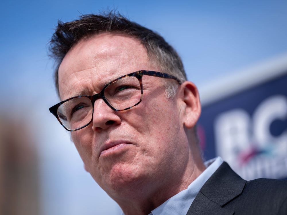 An light-skinned middle-aged man wearing a dress shirt and suit looks angry.