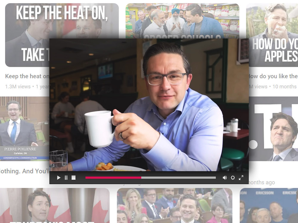 Pierre Poilievre is in a blue button-down shirt, holding up a white coffee cup while leaning over a breakfast plate at a diner. He smiles mischievously and has light skin, short dark hair and glasses.