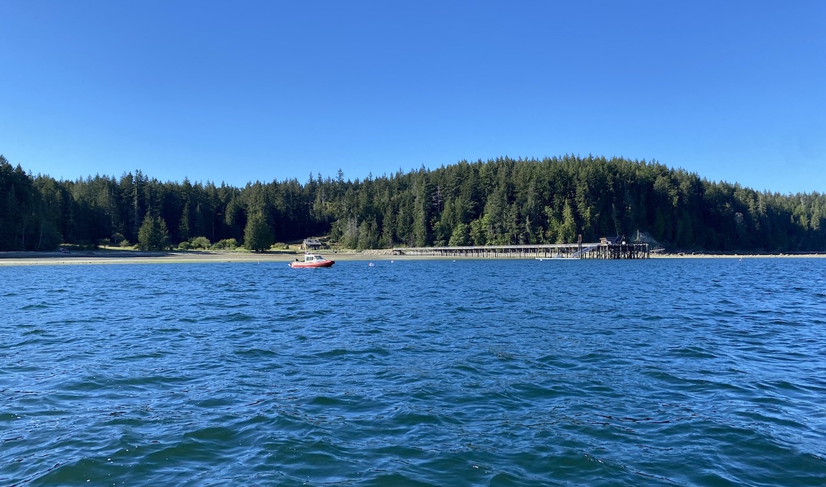 Hernando Island is wide and lined with trees. It is viewed from a boat on the water, which is blue and reflects the sky.