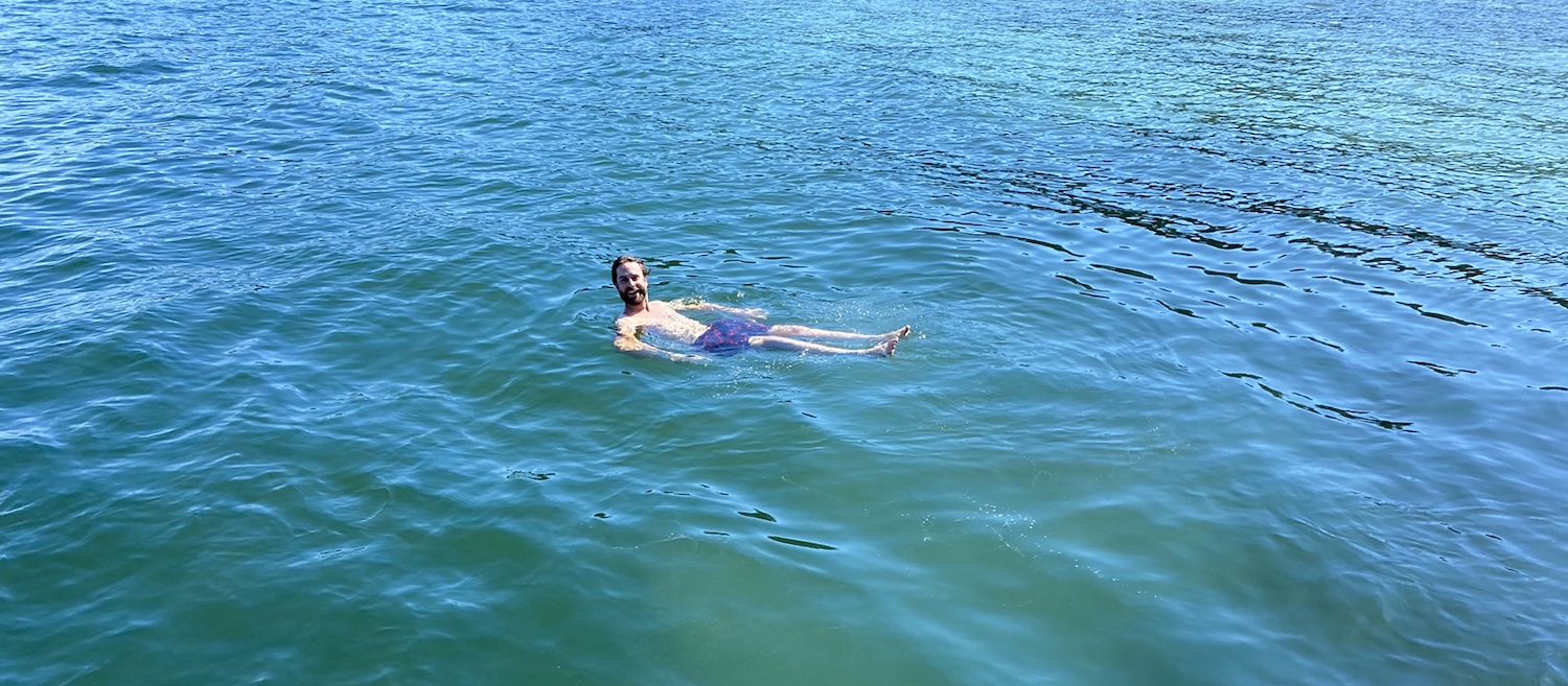 A man in blue swim trunks floats on his back in blue water.
