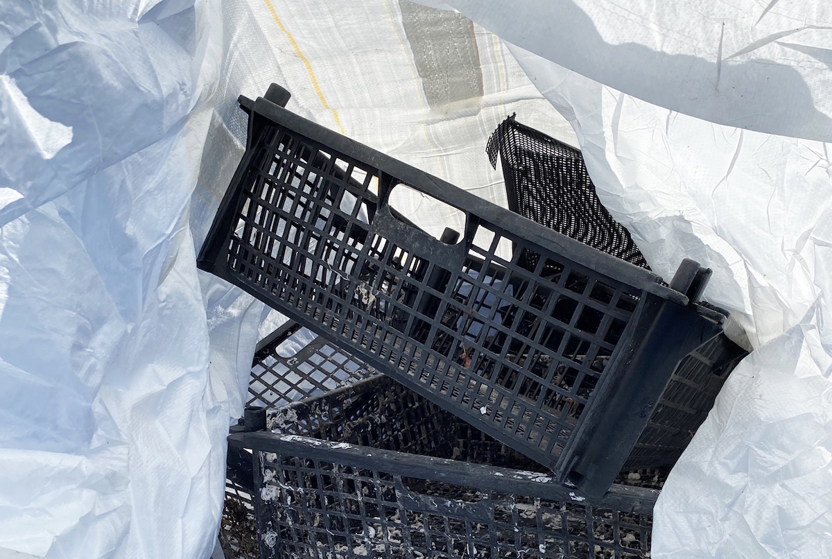 A small stack of black plastic baskets sit under the tent-like roof of a white bag covering them.