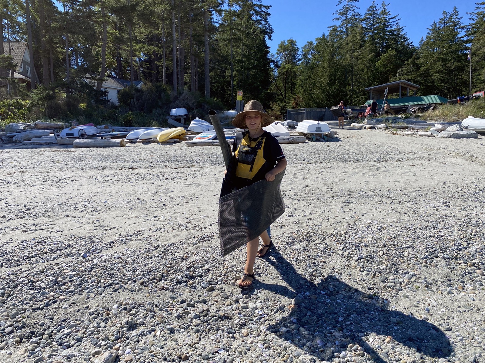 A young teen holds a large black piece of ocean debris as he walks along a rocky beach.