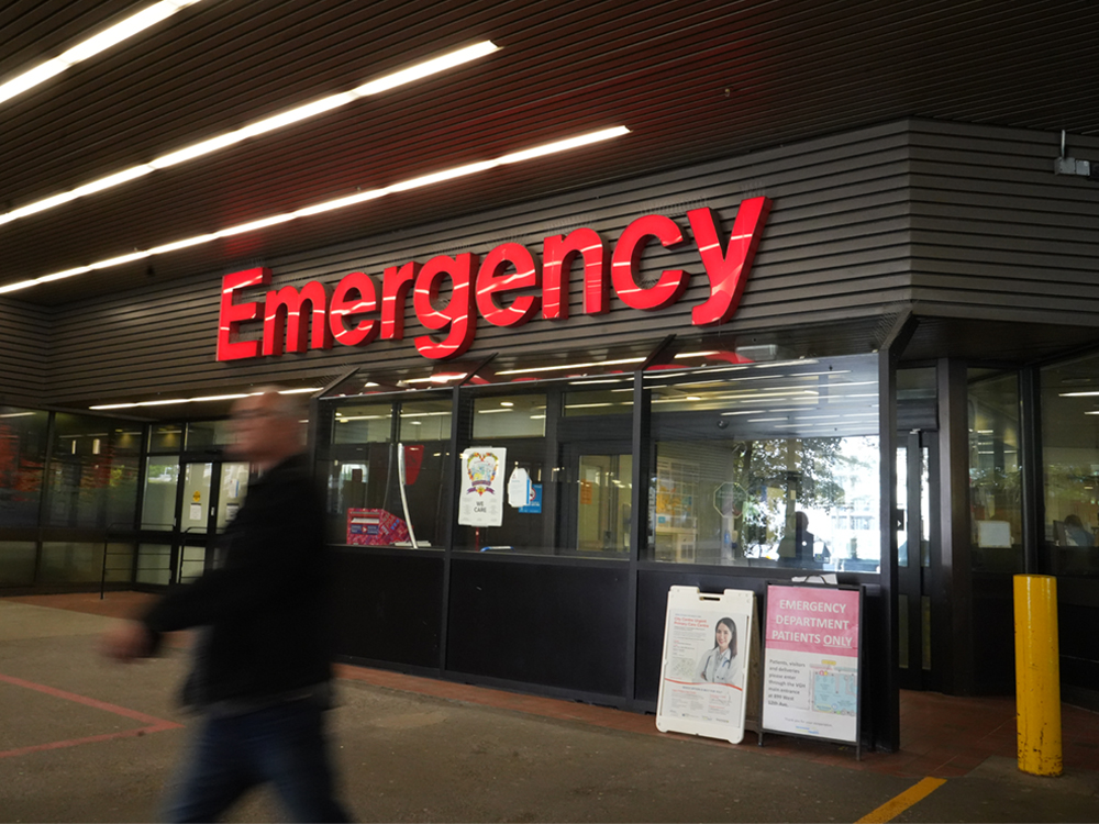 A man walks by an ER department with a bright red 'Emergency' sign.