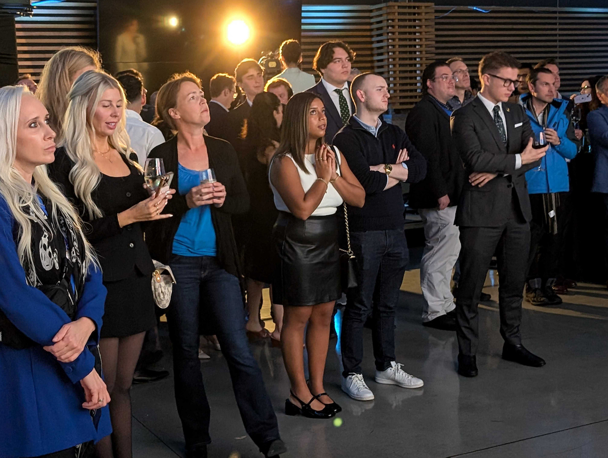 A group of people wearing blue, white and black watch the CBC livestream.