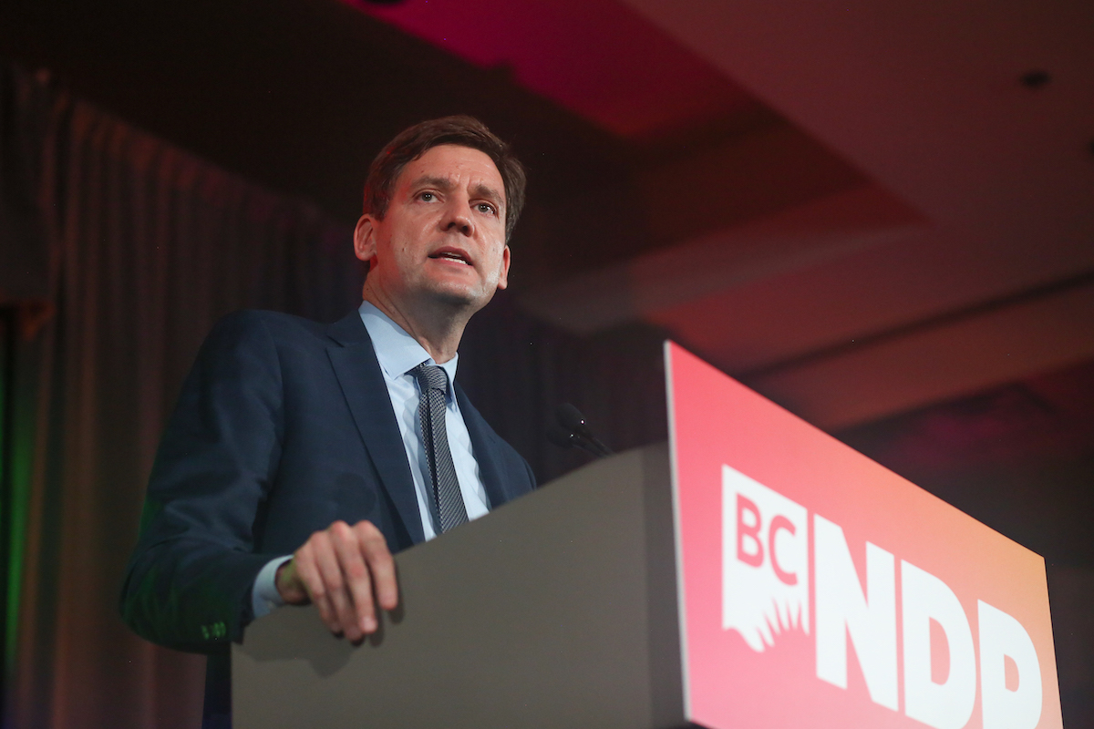 David Eby stands at a podium wearing a blazer and tie.