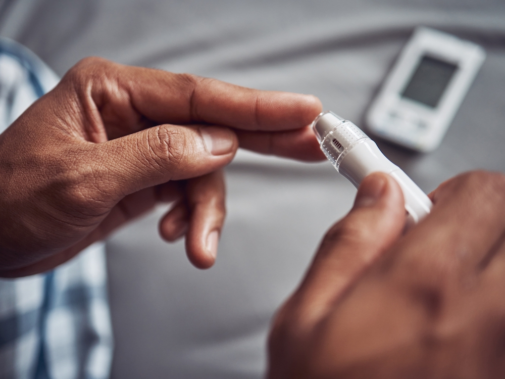 A close-up of a person with medium-dark skin about to take their glucose level with a finger prick.
