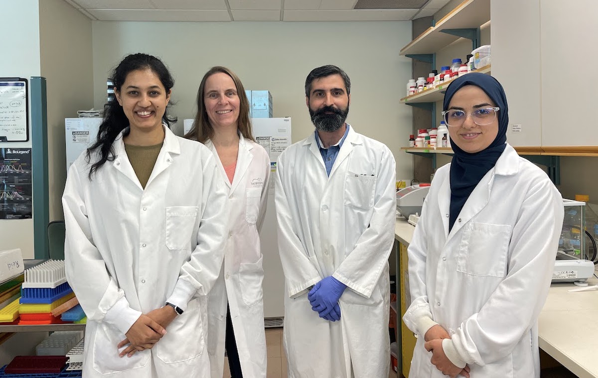 Four researchers wear white coats and stand in a lab.