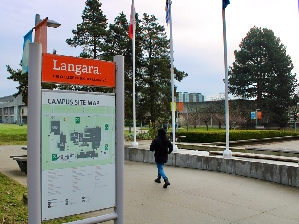 A person wearing jeans and a black coat walks by a Langara College campus map.