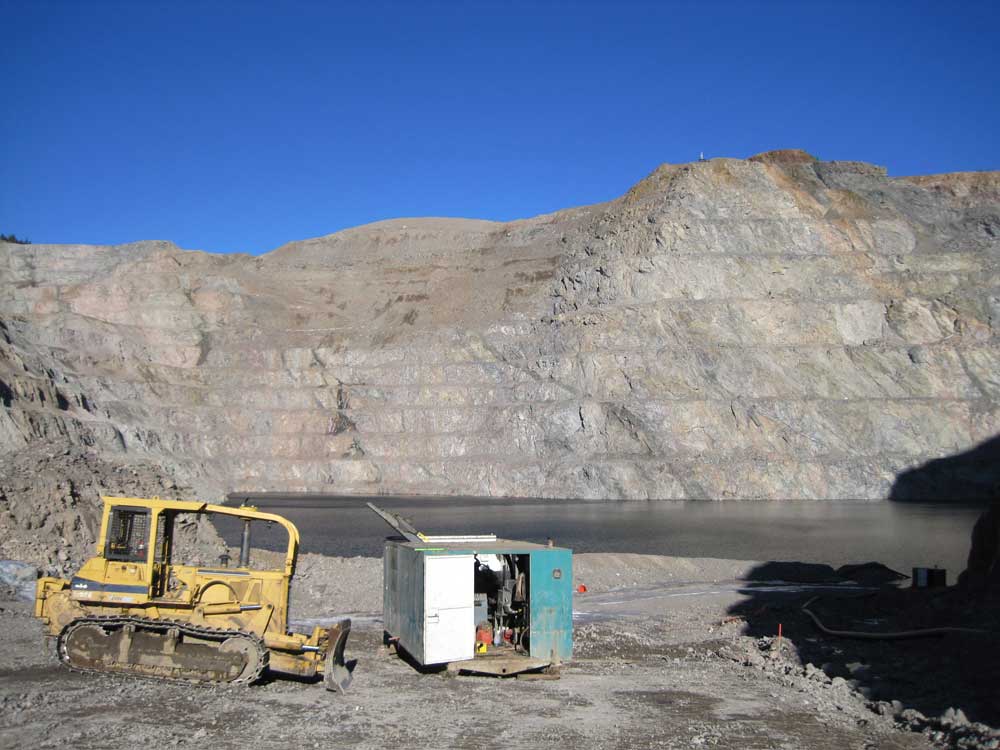 A blue sky above a stepped quarry filled with water.