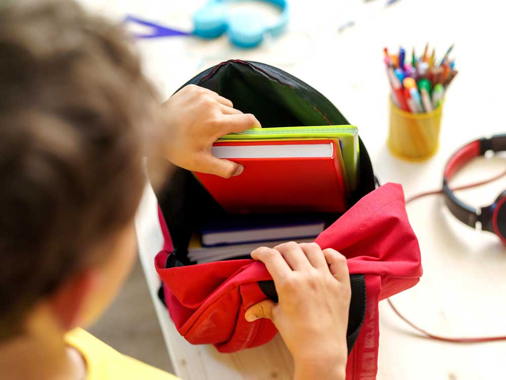A child places school-related objects into their backpack.