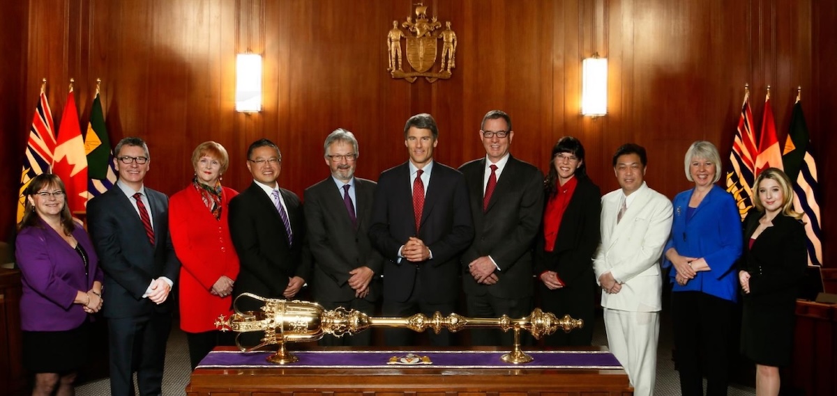 The 2014 Vancouver city council stands in chambers behind a large gold sceptre. Adriane Carr is second from right in a blue blazer.