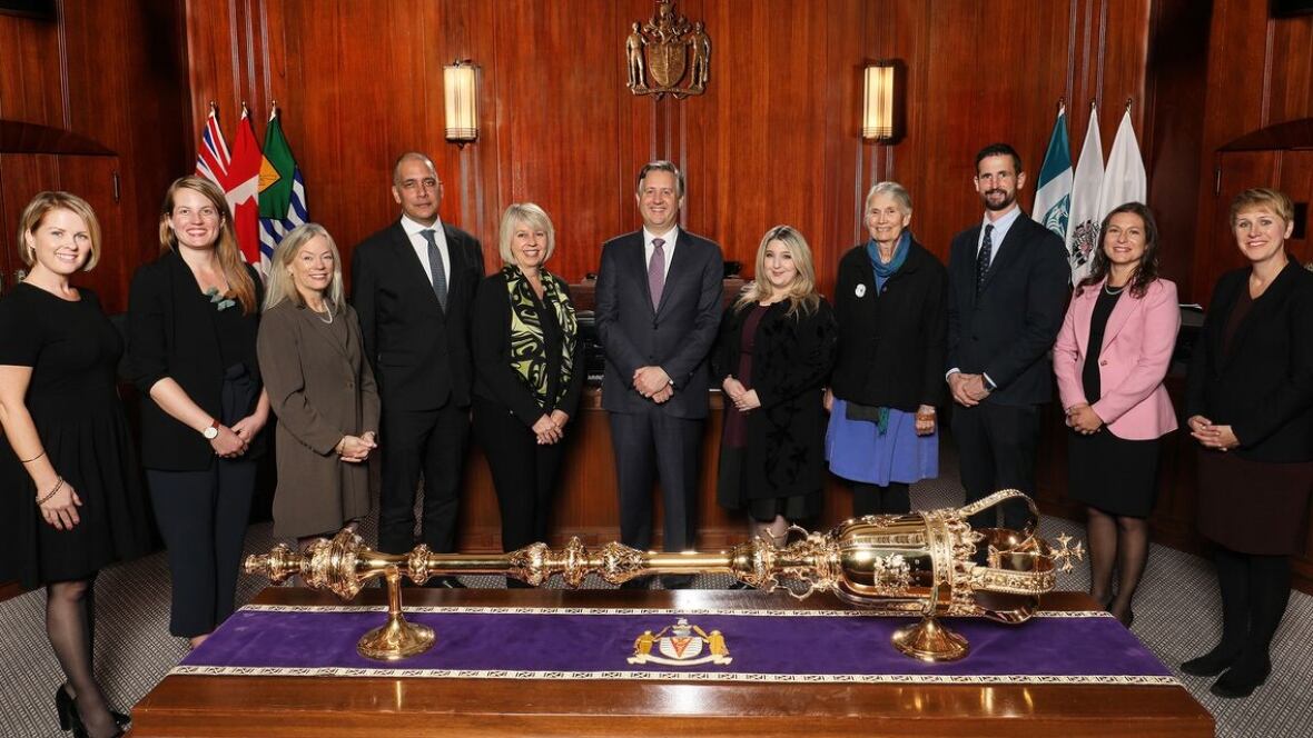 The 2018 Vancouver city council stands in chambers behind a gold sceptre. Adriane Carr is in the middle in a green scarf.