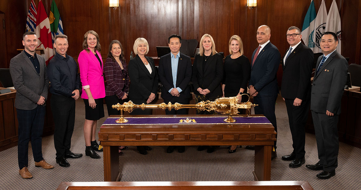 The 2022 Vancouver city council stands in chambers behind a gold sceptre. Adriane Carr is in the middle, to the left of Ken Sim, in a black blazer.