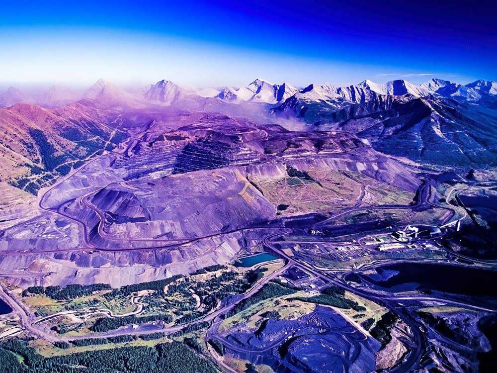 An aerial photo shows a heavily mined site with mountains in the background.