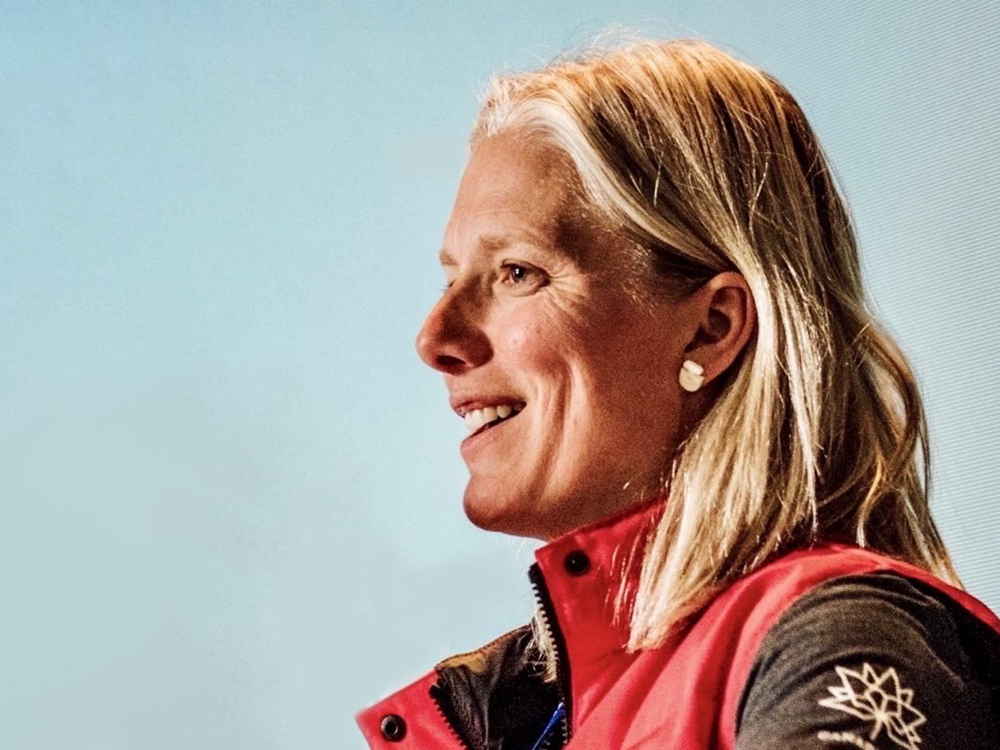 Catherine McKenna, a woman in her 50s with blond-grey hair and light skin tone, faces towards the left. She is wearing a Team Canada vest.