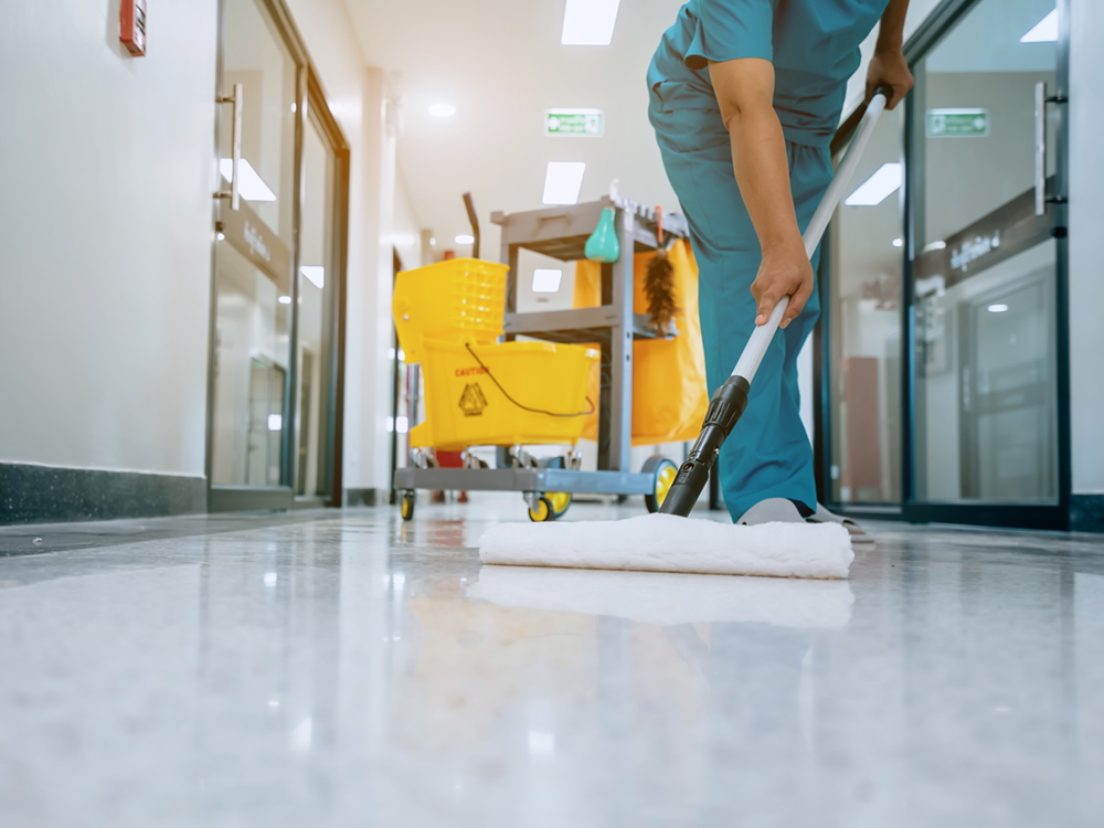 A person wearing teal-coloured scrubs mops a hospital hallway.