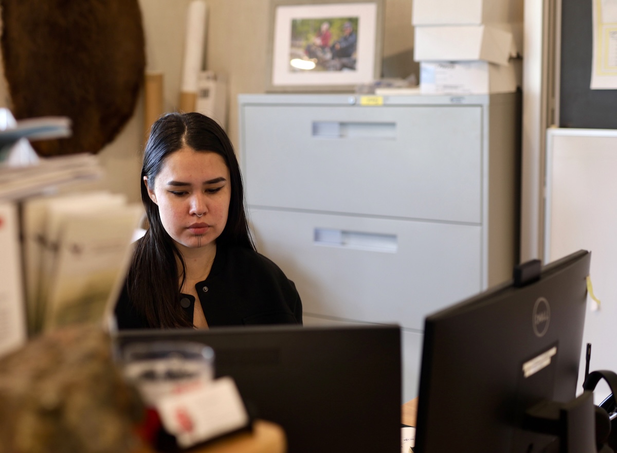 Kasandra Turbide, a young woman with long straight black hair and light skin, sits at a desk in an office space.