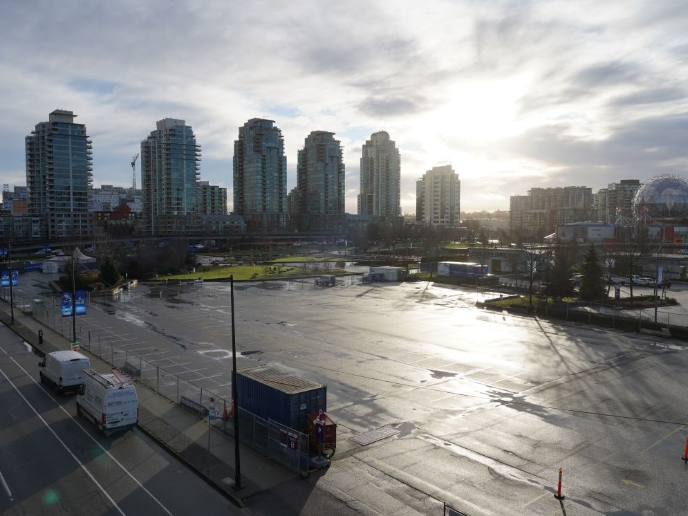 An empty parking lot with several highrise apartments visible in the background and the geodesic dome of Science World visible at far right.