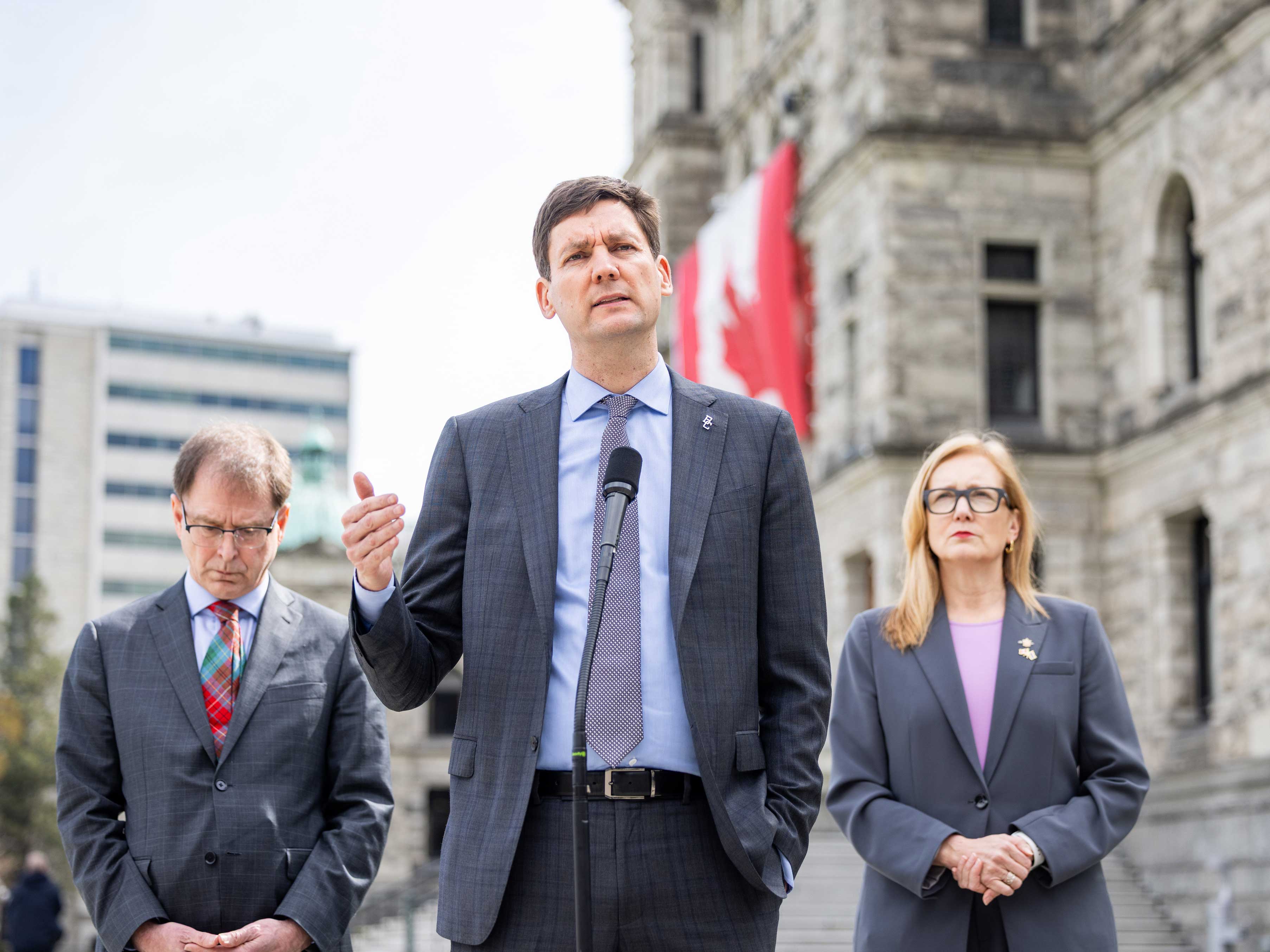 Premier David Eby stands outside, flanked by Adrian Dix on his left and Brenda Bailey on his right.
