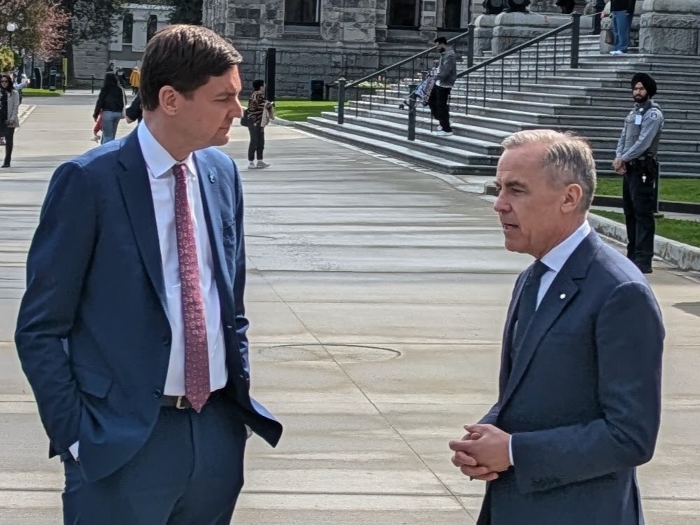 David Eby, a tall light-skinned man in a suit, stands facing Mark Carney, also in a suit, outside the B.C. Legislature.