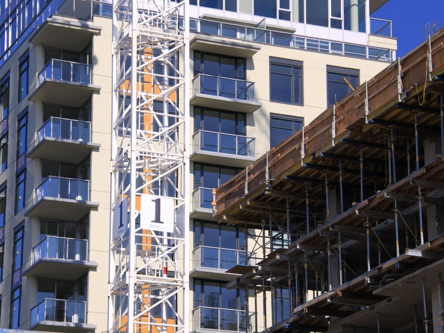 A crane stands in front of a partially completed housing highrise. In front, another building is in an earlier stage of construction.