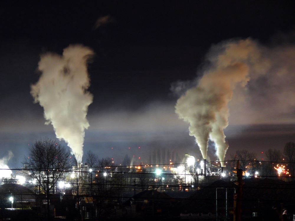 Twin white plumes rise in the night over a lit industrial compound.